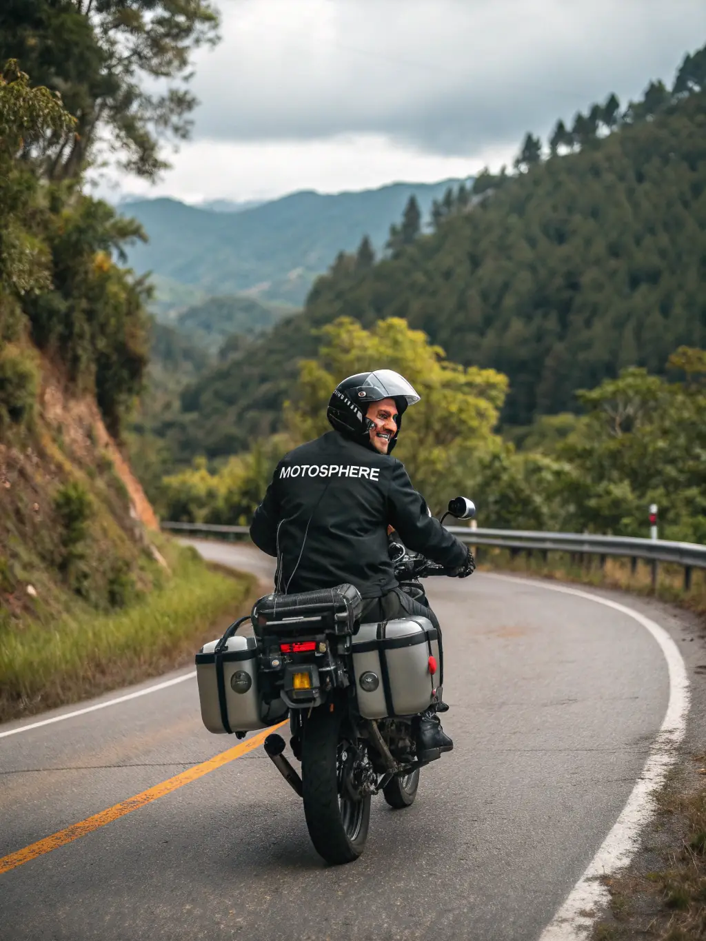 A motorcycle rider wearing a full touring jacket with multiple pockets, riding on a scenic highway with mountains in the background, showcasing the jacket's practicality and comfort.