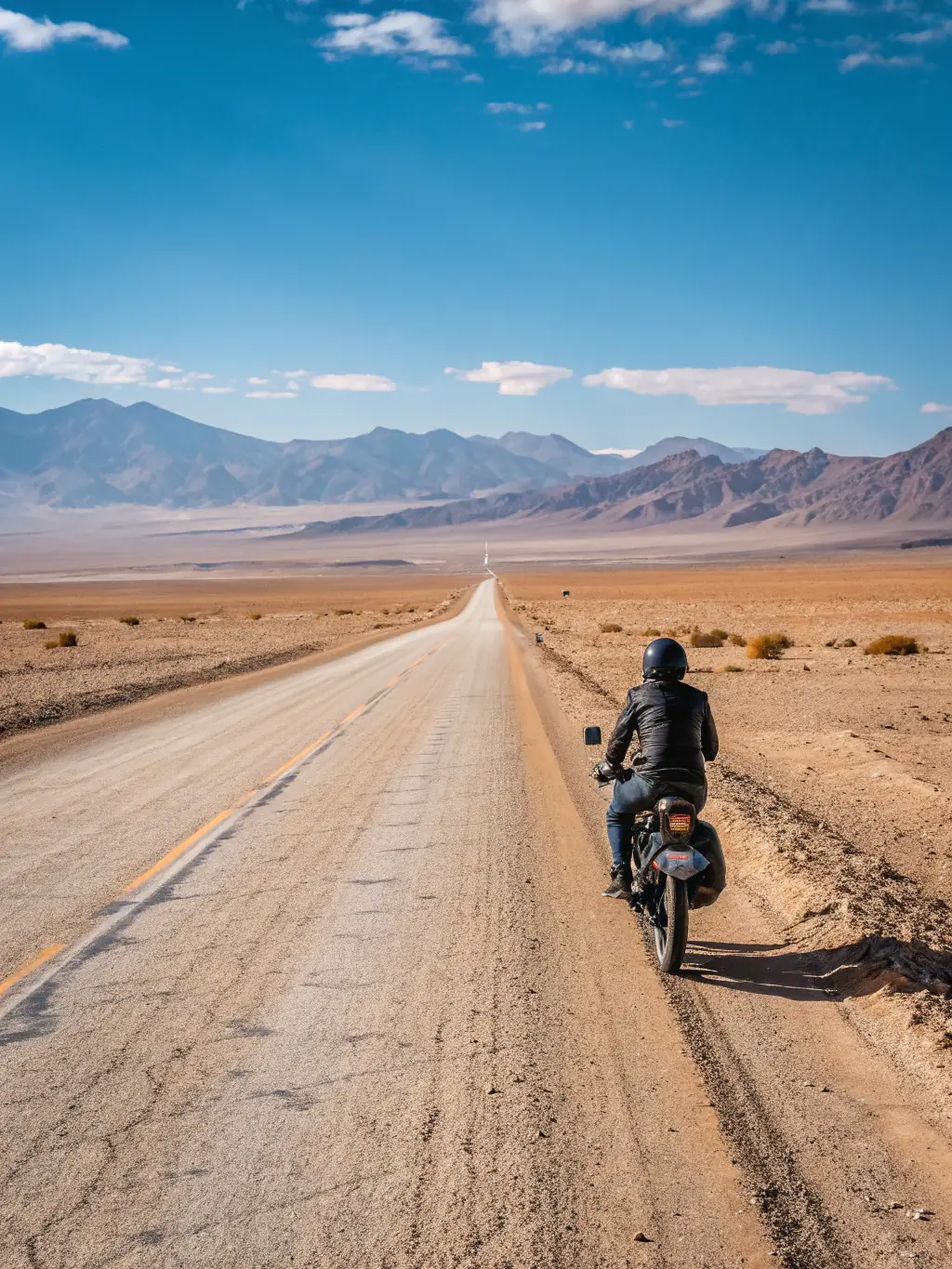 A rider wearing an armored adventure jacket standing next to their adventure motorcycle on a dirt road, showcasing the jacket's ruggedness and versatility.